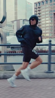 a man running in the city wearing a black hoodie and shorts with white sneakers