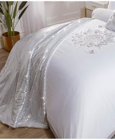 a white bed with silver sequins on it and a plant in the corner