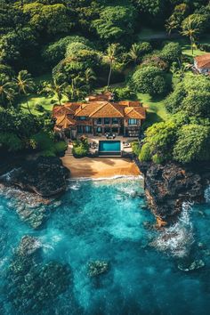 an aerial view of a house on the ocean with blue water and trees surrounding it