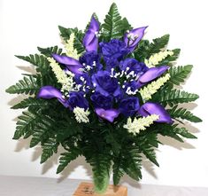 a vase filled with purple and white flowers on top of a wooden stand next to a wall