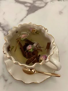 a white bowl filled with flowers on top of a marble counter next to a gold spoon