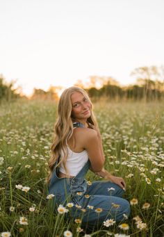 a woman sitting in the middle of a field with daisies