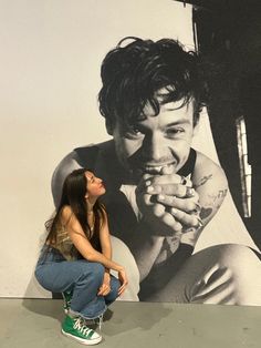 a woman sitting on the ground in front of a wall with a painting of a man