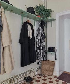 a coat rack with hats and coats hanging on it's sides, next to a tiled floor