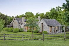 a large house in the middle of a lush green field next to a wooden fence