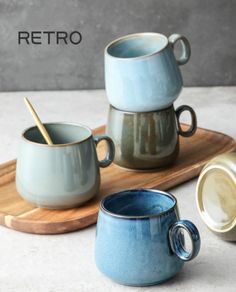 three mugs sitting on top of a wooden tray next to two cups with spoons in them