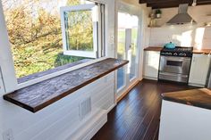 a kitchen with wood flooring and white cabinets next to an open window that looks out onto the woods