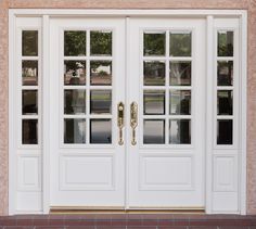 two white double doors with glass panes in front of a brick wall and sidewalk