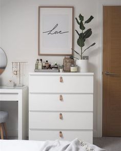 a white dresser sitting next to a bed with a plant on top of it in a bedroom