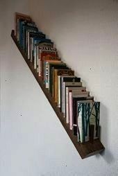 the books are lined up on the wall by the stair case, which is made out of wood