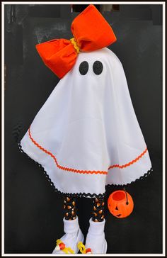 a white halloween ghost with orange bow and pumpkins on it's feet, standing in front of a black door