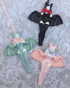 three ornaments are hanging on a lace tablecloth, one has a bat and the other is a cat