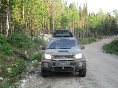 a truck is parked on the side of a dirt road in front of some trees