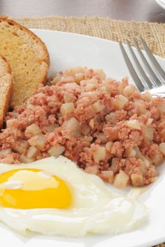 a white plate topped with meat and eggs next to two slices of bread on top of a table