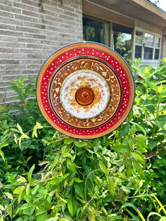 a red and yellow plate hanging from a tree in front of a brick building with green bushes