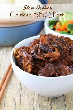 a bowl filled with beef and vegetables next to chopsticks on a wooden table