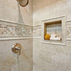 a bathroom with white tile walls and tan tiles on the shower wall, along with a gold faucet