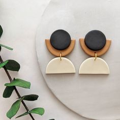 two tone earrings with black stone and wood accents on a white plate next to greenery