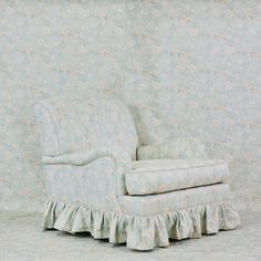 an old chair with ruffled cushions against a floral wallpaper