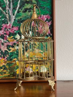 a golden birdcage sitting on top of a wooden table next to a painting