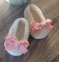 two crocheted baby shoes with pink bows sit on a table next to a vase