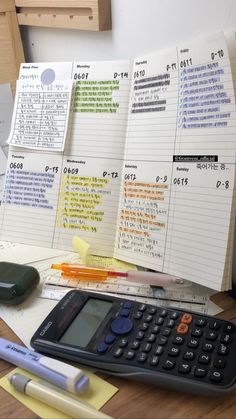 a calculator sitting on top of a wooden table next to papers and pens