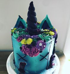 there is a blue cake decorated with flowers and a unicorn horn on the top tier