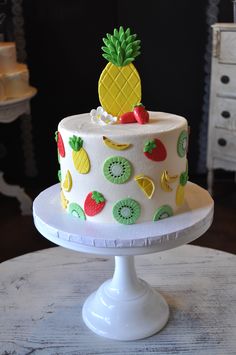 a white cake with pineapples and kiwi slices on it sitting on a pedestal