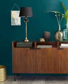 a sideboard with two vases and a lamp on it in front of a green wall