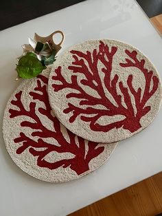 two red coral placemats sitting on top of a white counter next to a plant