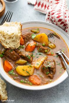 a bowl of beef stew with bread on the side