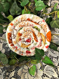 an orange and white plate sitting on top of some green leafy plants next to a lace doily