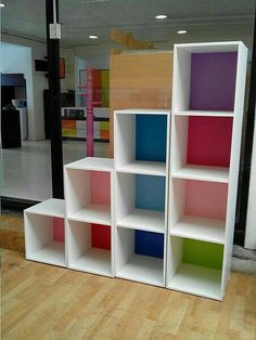 four different colored bookshelves sitting on top of a hard wood floor in front of a store window