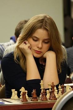 a woman sitting at a table with her hand on her head while playing the game of chess