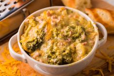 a casserole dish with broccoli, cheese and bread in the background