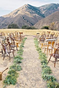 rows of wooden chairs sitting on top of a dry grass covered field with mountains in the background