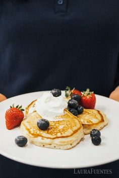 a person holding a plate with pancakes and strawberries on it