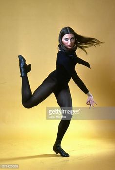 a woman in black bodysuit posing with her legs spread out and one leg up