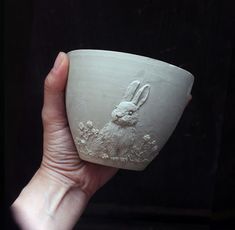 a hand holding a white ceramic cup with a rabbit on it