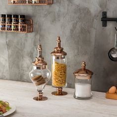 three glass jars filled with food sitting on top of a counter next to plates and utensils