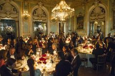 a large group of people sitting at tables in a fancy room with chandeliers