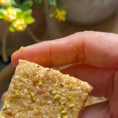 a hand holding a piece of food in it's left hand, with flowers in the background