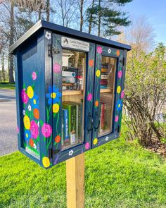 a blue mailbox with flowers painted on it in the grass next to a street