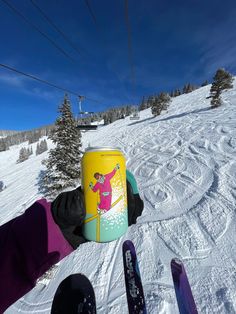 a person holding up a can on top of a snow covered slope with skis