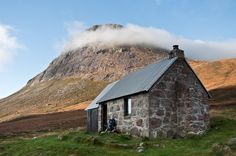 a small stone building sitting on top of a lush green field next to a mountain