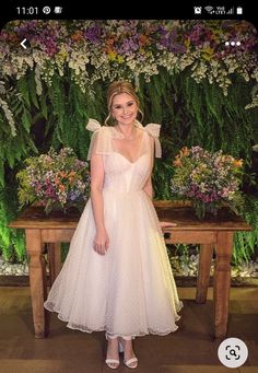 a woman in a white dress standing next to a wooden table with flowers on it