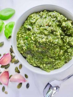 a white bowl filled with green pesto next to flowers and spoons on a table