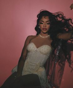 a woman sitting on top of a chair in front of a pink wall with long hair