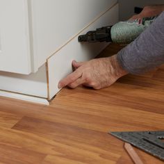 a man is using a drill to install the baseboard on a wall in his home