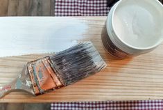 a paint can and brush sitting on top of a wooden table next to a white cup